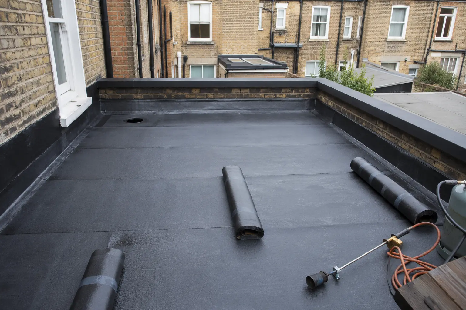 A flat roof mid-installation with membrane being laid across a clean timber deck